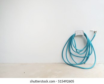 A Garden Hose Keep On The White Concrete Wall.