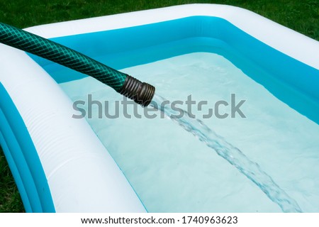 A garden hose pours water to fill a backyard inflatable swimming pool. 