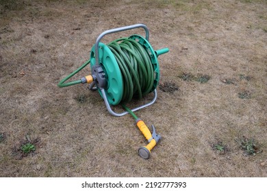 Garden hose reel sitting unused on a dry lawn. Hosepipe ban in UK due to drought. - Shutterstock ID 2192777393