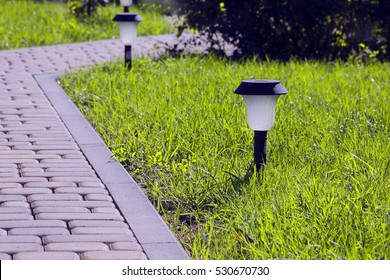 Garden Lighting - Lights On The Solar Battery On A Green Lawn Next To A Paved Path