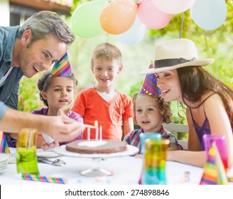 Garden Party With Family For Little Girl's Birthday, Dad Lights The Candles On The Cake , The Garden Is Decorated With Balloons And Colors Are Bright