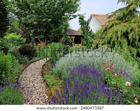 A garden path made of pebbles lined with lavender and flowers in an ornamental garden in the village of Klapý in the Czech Republic in Europe. There are lots of flowers, bushes and trees. 