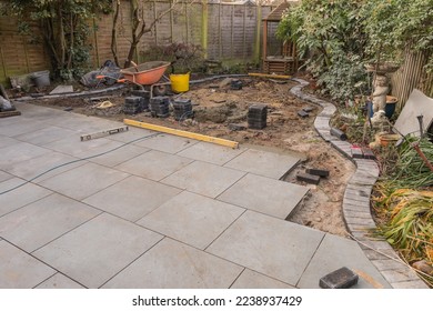 Garden paving under construction, with grey porcelain patio tiles and curved charcoal edge bricks.