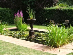 A Garden Pond With Statuary And Plants.