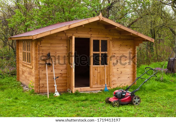 Garden shed with
hoe, string trimmer,  rake and grass-cutter. Gardening tools shed.
Garden house on lawn in garden. Wooden tool-shed. Hovel made of
timber in domestic environment.
