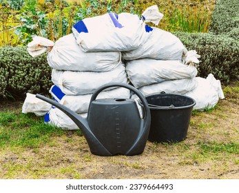 Garden tools, watering can, bucket, bags with fertilizer on the background of plants. Autumn gardening