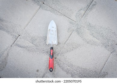 Garden Trowel With Polymeric Paver Sand On Top Of Gray Concrete Patio Stone Paver Walkway. This Material To Fill Joint Between Pavers To Firm And Prevent Weeds From Growing Up Between