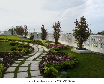 Garden With Walkway And White Fence. Cloudy Sky Above The Horizon And The Sea.