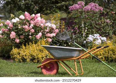 A garden wheelbarrow and a rake in the backyard of the house. The concept of housework, gardening and country life. Preparing the garden for autumn and winter. Closing of the summer season. - Powered by Shutterstock