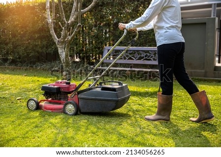 Garden work on the care of the lawn. A woman mows the lawn using an electric pushing lawn mower.. cleaning concept