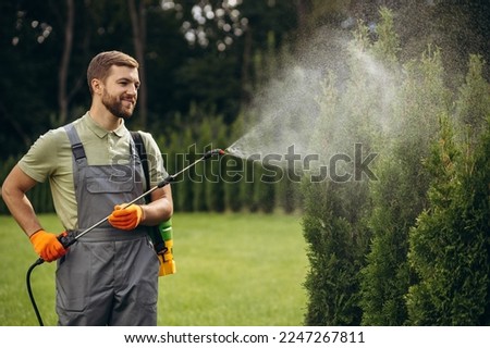 Garden worker watering grass and bushes in the yard with sprinkler