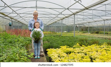 Gardener And Grandddaughter In The Greenhouse Holding Large Potted Plant