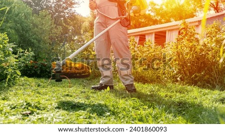 a gardener with a grass trimmer mows the lawn. High quality photo