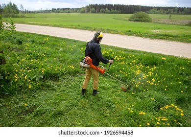 The gardener man mows the grass with yellow dandelions with a hand lawn mower. close up hands trimmer, selective focus - Shutterstock ID 1926594458