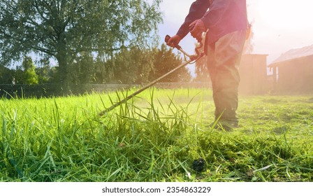 Gardener mows weeds grass. Man cutting grass in yard by using string trimmer. Worker lawn mower cutting green garden. Lawn mowing machine. Grass Trimmer and Grass Cutter. lawn maintenance service.