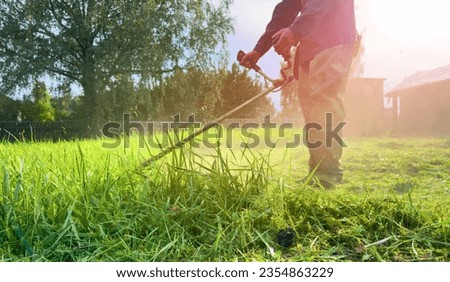 Gardener mows weeds grass. Man cutting grass in yard by using string trimmer. Worker lawn mower cutting green garden. Lawn mowing machine. Grass Trimmer and Grass Cutter. lawn maintenance service.