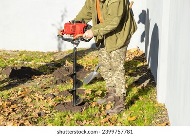 Gardener using tools hand-held soil hole drilling machine or portable manual earth auger for prepare the soil for planting shrubs or trees.
