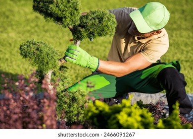 Gardener wearing a green hat is actively trimming a tree with a tool in a focused manner. - Powered by Shutterstock