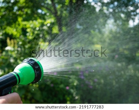 Gardener's hand holds a hose with a sprayer and watered the plants in the garden.