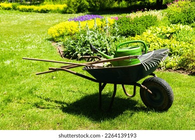 A gardeners wheelbarrow with the gardening tools in the gardens. Gardening concept - Shutterstock ID 2264139193