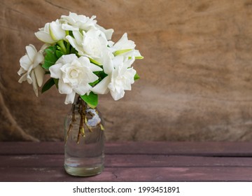 Gardenia Bouquet In A Glass Bottle Put On Wooden Table Against Wooden Background.