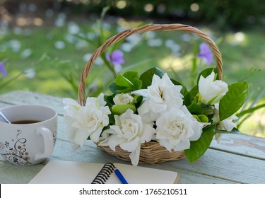 Gardenia Bouquet In The Wicker Basket And Note Book, Pencil ,cup Of Coffee That All Of Them Put On The Wooden Table In The Home Garden.