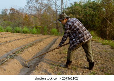 Gardening concept a male farmer using a hoe digging to the soil for making vegetable plots preparing for growing the plants. - Shutterstock ID 2093611024