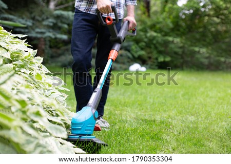 Gardening. Cutting the lawn with cordless grass trimmer, edger, close-up.