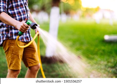 Gardening And Maintainance- Close Up Of Man Hands With Hose Watering The Lawn