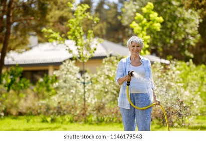 Gardening And People Concept - Happy Senior Woman Watering Lawn By Garden Hose At Summer