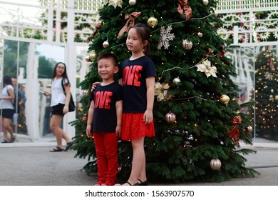 Gardens By The Bay / Singapore - DECEMBER 8, 2018: Boy Girl Siblings Friends Posing In Front Of Christmas Tree Smiling Happily