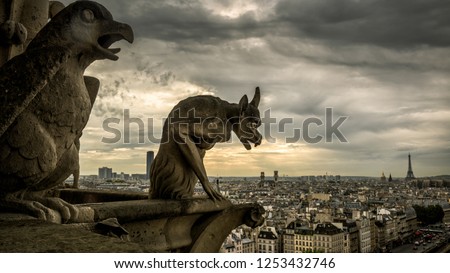 Gargoyles or chimeras on Cathedral of Notre Dame de Paris overlooking city, France. Gargoyles are Gothic landmark of Paris. Dramatic dark skyline, fantasy demon statue on church roof against sky.