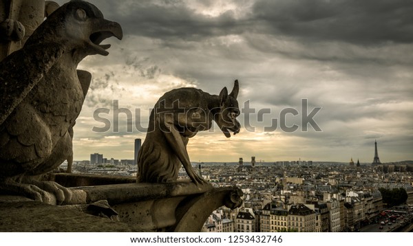 Gargoyles or chimeras on Cathedral of Notre Dame de\
Paris overlooking city, France. Gargoyles are Gothic landmark of\
Paris. Dramatic dark skyline, fantasy demon statue on church roof\
against sky.