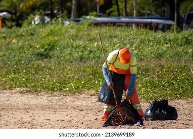 Gari cleaning the beach sand using a rake. Man throws dirt into garbage bag