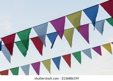 Garland of colorful flags of triangular shape, pennants against blue sky. City street holiday. Modern background, pattern, wallpaper or banner design. Fest, celebration concept