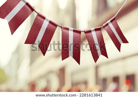 A garland of Latvia national flags on an abstract blurred background.