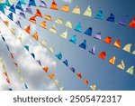 A garland of multi-colored flags against the background of a blue sky with white clouds. A festive decoration of the city.