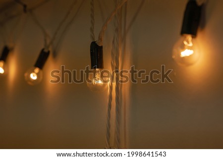 Garland with round small bulbs with black base glowing with warm orange light hang on a white wall in a dark room. Loft-style decor. Close-up. Evening