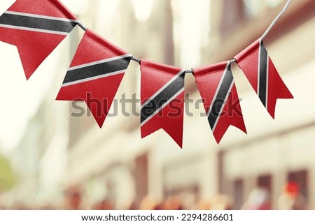A garland of Trinidad and Tobago national flags on an abstract blurred background.