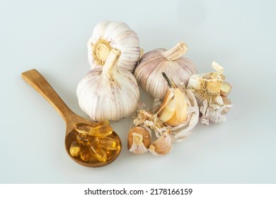 Garlic Bulbs ( Allium Sativum L.) And Garlic Cloves With Capsules Of Oil In Wooden Spoon And On White Background. Garlic Prevents Heart Disease And Reduces The Risk Of Acute Heart Failure.