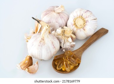 Garlic Bulbs ( Allium Sativum L.) And Garlic Cloves With Capsules Of Oil In Wooden Spoon And On White Background. Garlic Prevents Heart Disease And Reduces The Risk Of Acute Heart Failure.