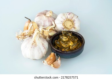 Garlic Bulbs ( Allium Sativum L.) And Garlic Cloves With Capsules Of Oil In Ceramic Bowl And On White Background. Garlic Prevents Heart Disease And Reduces The Risk Of Acute Heart Failure.