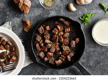 Garlic butter steak bites in frying pan over dark stone background. Top view, flat lay