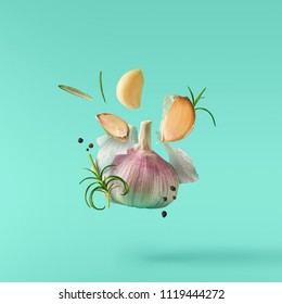 Garlic falling in air with pepper and herbs like rosemary on turquoise background. Spicy food concept - Powered by Shutterstock