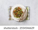 garlic green bean stir fry with crispy tofu on a bed of white jasmine rice in white bowl with chopsticks on white concrete table, horizontal view from above, flat lay