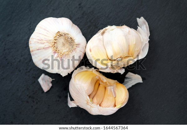 Garlic on a black background top view. Two heads\
of garlic, one whole, the other divided in half. Dry garlic with\
yellow edges.