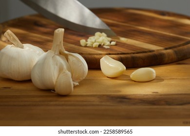  garlic on a wooden chopping board close-up. a knife grinds a clove of garlic surrounded by whole ones. kitchen on a sunny day. High quality photo - Shutterstock ID 2258589565