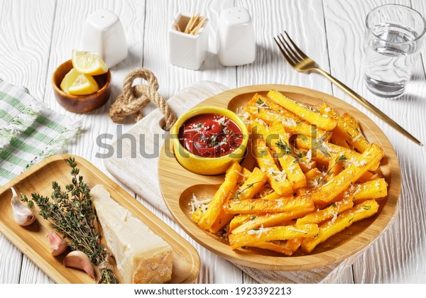 garlic parmesan polenta fries with parmesan\
cheese, thyme and spices in a bamboo dish with tomato sauce on a\
white wooden table, italy\
cuisine