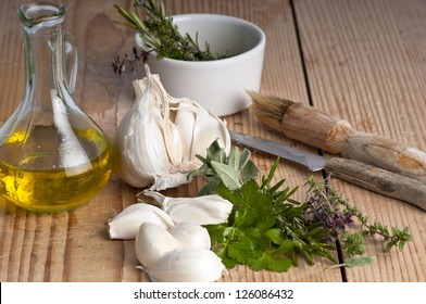 Garlic, parsley, sage, rosemary and thyme with extra virgin olive oil in  a jug, a brush and knife. on an antique chopping board.