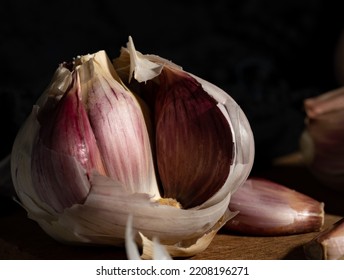 A Garlic Resting On A Wooden Board. The Garlic Is In The Foreground And You Can See Inside.